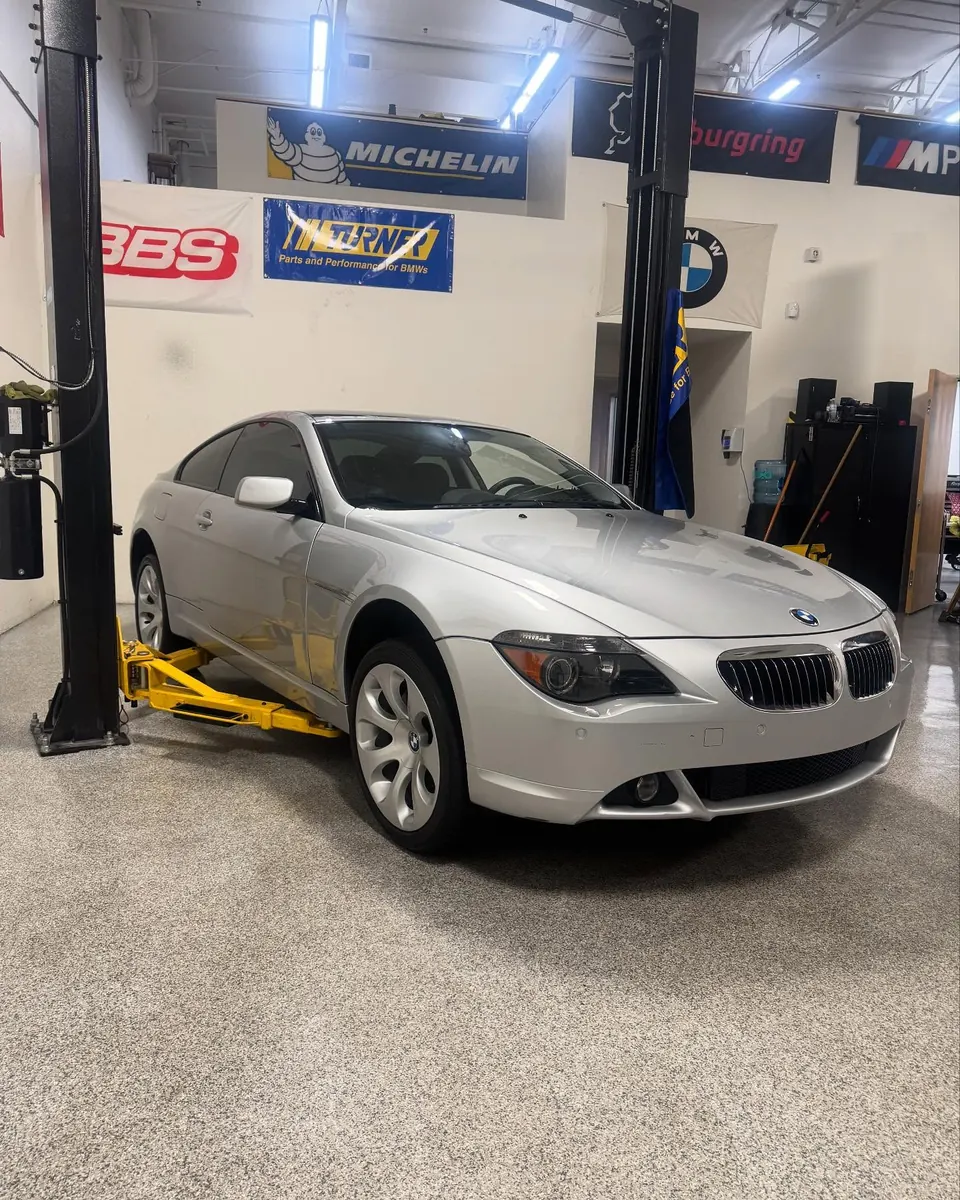 A manual BMW 645Ci on a lift in the EuroWorks shop, under BBS, Michelin and BMW banners